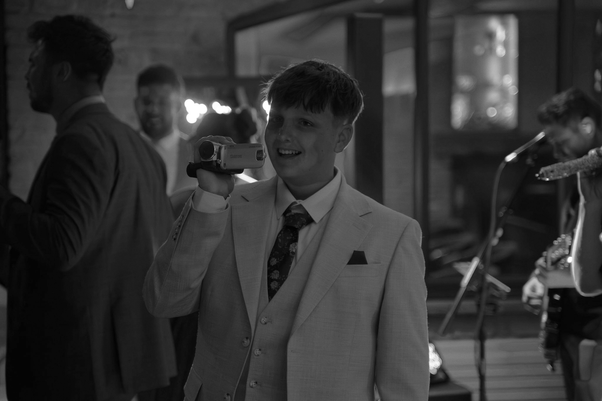 Wedding guest filming on a vintage camcorder at a real UK wedding reception, capturing candid unscripted moments as an alternative wedding video.
